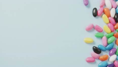 Video-of-overhead-view-of-multi-coloured-sweets-with-copy-space-over-blue-background