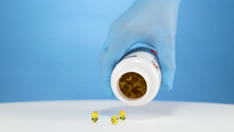 Hand-with-blue-glove-empties-omega-vitamin-capsules,-studio-with-blue-background