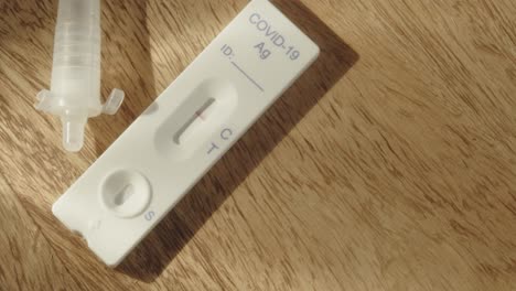 Pan-across-COVID-19-antigen-test-on-wood-table,-high-angle